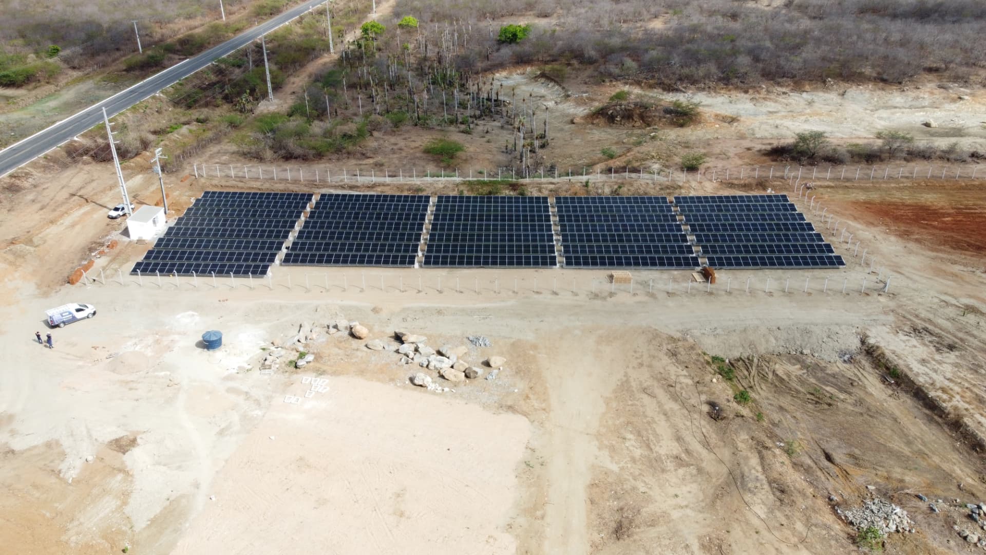 Vista aérea de fileiras de módulos fotovoltaicos instalados em terreno cercado